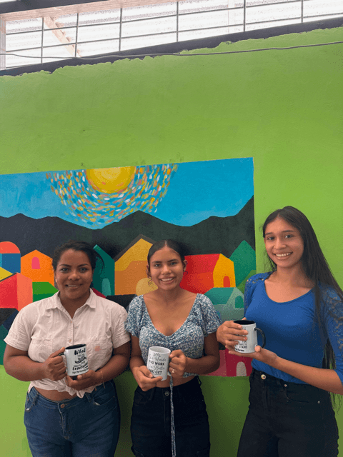 Adriana, Greyling, and Magaly standing together with motivational mugs at the Community Center