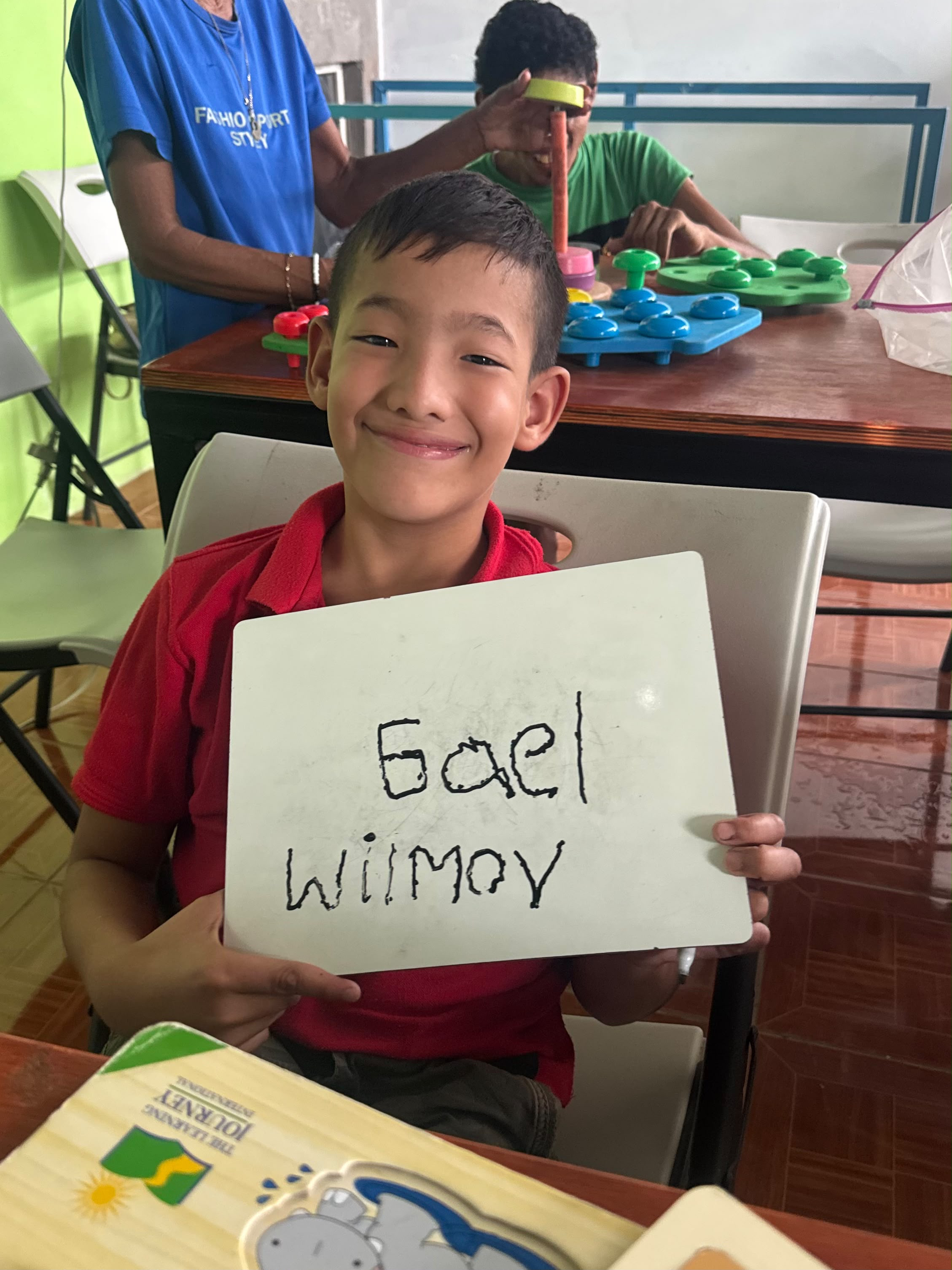 Gael holding up a whiteboard with his name and his teacher's name written on it